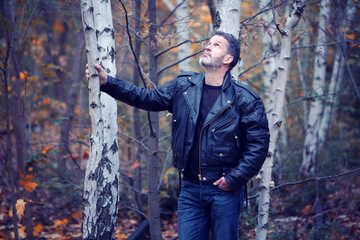 Fototapeta na wymiar handsome man in leather jacket standing in forest