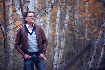 Naklejka na ściany i meble man in his 50s in brown leather jacket standing in forest
