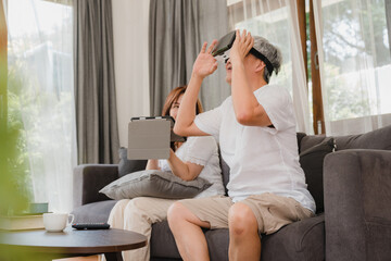 Obraz na płótnie Canvas Asian elderly couple using tablet and virtual reality simulator playing games in living room, couple feeling happy using time together lying on sofa at home. Lifestyle Senior family at home concept.