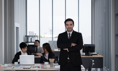 portrait of young caucasian businessman standing in office with background multiethnic colleagues working together. business concept