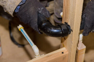 Plumbing building contractor installing plastic drain pipe in the elbow for sink drain for a custom...