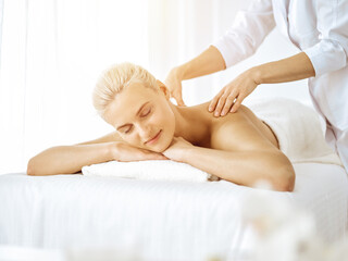 Obraz na płótnie Canvas Beautiful blonde woman enjoying back massage with closed eyes in sunny spa salon. Beauty concept