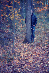 man in black leather jacket standing behind tree in forest