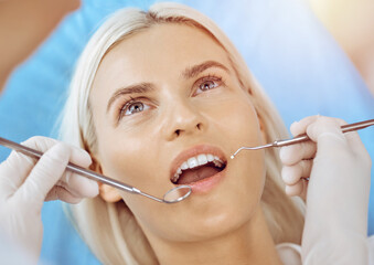 Smiling blonde woman examined by dentist at sunny dental clinic. Healthy teeth and medicine concept