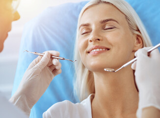 Smiling blonde woman examined by dentist at sunny dental clinic. Healthy teeth and medicine concept