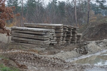 a pile of old gray concrete slabs lie in the mud near a puddle among trees on the street