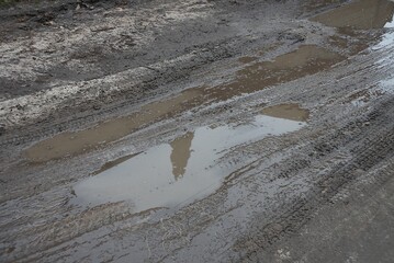 one big  puddle with brown dirty water on the gray ground of a rural road