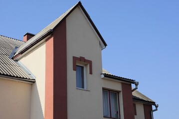 gray brown concrete attic of a private house with a window under a slate roof against a blue sky
