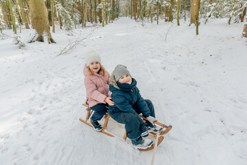 2 children sit on a wooden sledge and smile. Children in winter clothes. Winter in East Frisia. Snow in Germany 