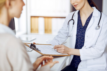 Doctor and patient discussing current health examination while sitting in sunny clinic. Medicine...