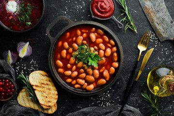 Boiled beans in tomato sauce with parsley and spices in a black metal pan. Rustic style. Top view.