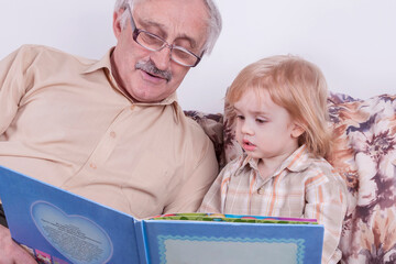 The grandfather reads a book for his grandson.  The grandson listens enthusiastically to the...
