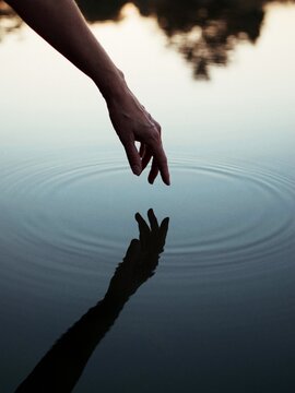 Person's hand touching body of water with reflection