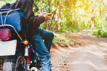 A young male tourist driving a motorbike on a dirt road in the forest is using a mobile phone.