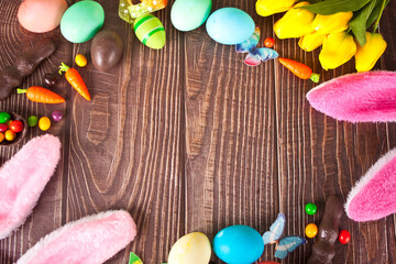 Easter set frame with eggs, tulips, bunny ears, carrots on the wooden background. Top view. Copy space.
