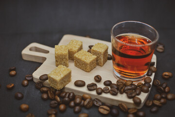 An alcoholic drink in a glass stands on a wooden board and coffee beans are scattered next to it .