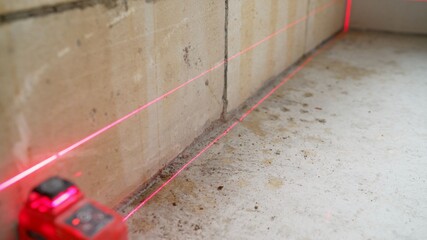 Close-up of modern engineering device set on the floor, installation of laser level for measurement on renovation site. Laser red rays creating horizontal crosshair for accurate measures. 