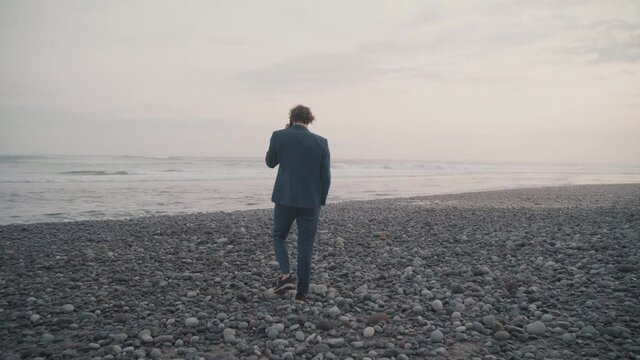 Drone shot of successful business man on trip in bali, having phone conversation walking along isolated ocean coast