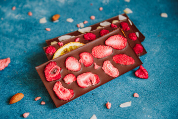 Diet dark chocolate without sugar based on cocoa and stevia with the addition of freeze-dried berries, nuts and fruits. Top view on blue background