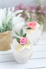 Several cupcakes and muffins with white butter cream and a lively pink rose on a white wooden table. Valentine's day or Mother's Day gift. Fresh flowers are on the table nearby. Rustic style.