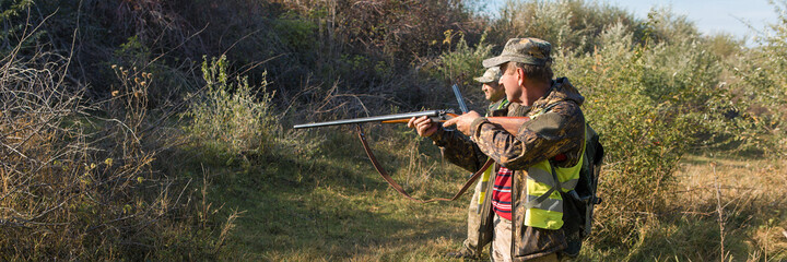 Fototapeta premium Hunter man in camouflage with a gun during the hunt in search of wild birds or game.