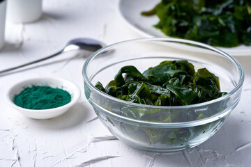 close up laminaria (Kelp) seaweed and spirulina powder in a glasses bowl with a wooden spoon on white background                                                              