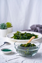 laminaria (Kelp) seaweed and spirulina powder in a glasses bowl with a wooden spoon on white background. vertical                                                                          