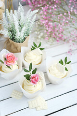 Several cupcakes and muffins with white butter cream and a lively pink rose on a white wooden table. Valentine's day or Mother's Day gift. Fresh flowers are on the table nearby. Rustic style.