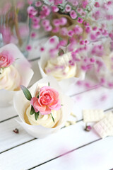 Obraz na płótnie Canvas Several cupcakes and muffins with white butter cream and a lively pink rose on a white wooden table. Valentine's day or Mother's Day gift. Fresh flowers are on the table nearby. Rustic style.