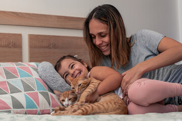 Mother, daughter and their cat, playing on the bed at home.
