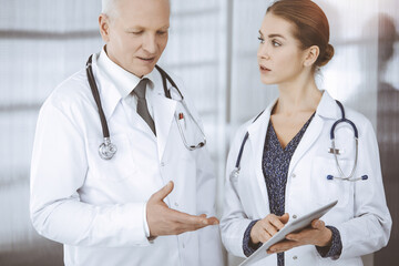Elderly confident doctor and woman-physician discussing current disease therapy while standing in...