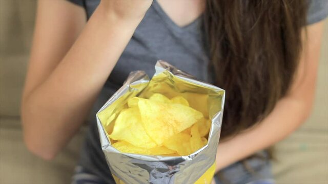 Young girl sitting on the sofa and eating chips from packet