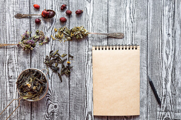 Dry herbal tea and empty notebook with pencil. Chamaenerion, chamomile, Oríganum and Filipendula on gray wooden with place for text