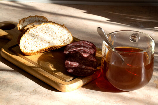 A cup of tea with bread and kalbasa on a wooden board.