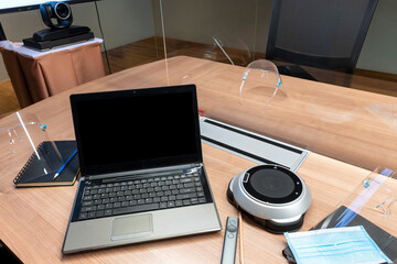 Laptop display blank and face shield ,mask on table in meeting room with clear acrylic sheet separates the center on the conference table to prevent COVID-19