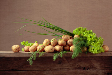 Young fresh organic potatoes with dill, salad and onion on a old wooden table.