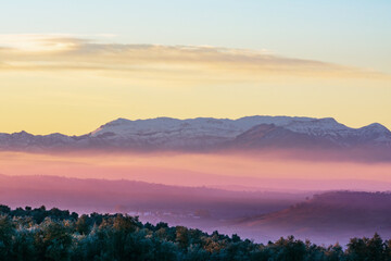 Obraz premium Landscape of Sierra Morena de Jaen, located in the northern region of Linares, with snow-capped mountains and the morning mist colored by the sun.