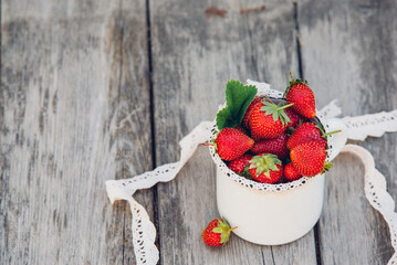 Fresh juicy strawberries with leaves. Rustic enameled mug and handmade lace. Retro magazine picture.