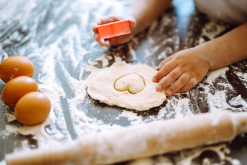 Close up of boy hands carving dough with cookie heart cutters. Easter baking preparation. A little chef carves ginger Cookies.