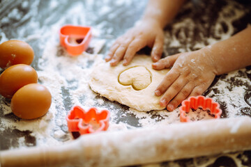 Close up of boy hands carving dough with cookie heart cutters. Easter baking preparation. A little chef carves ginger Cookies.