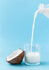coconut milk is poured from a bottle into a glass. coconut and glass with milk on a blue background