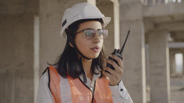 close view shot of a young Indian asian woman civil engineer talking on walkie talkie on top of a under development building near a construction site