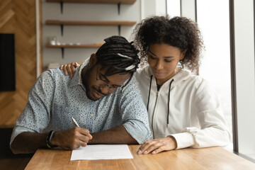 Focused young black couple signing prenuptial agreement in lawyer office. Concentrated millennial...