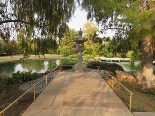 A stone sculpture in a tranquil  Japanese garden with trees, plants, and a Koi fish pond located in...