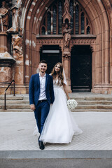 A romantic walk of the bride and groom through the city streets. Newlyweds on the background of the cathedral.