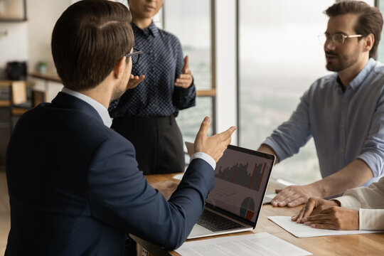 Over shoulder view of young businessman take part in corporate meeting propose decision based on data at laptop screen. Diverse business team discuss statistical report infographics charts share ideas