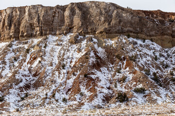 Side of tall red rock mountain covered in snow on overcast day in rural New Mexico