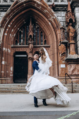Obraz premium A romantic walk of the bride and groom through the city streets. Newlyweds on the background of the cathedral.