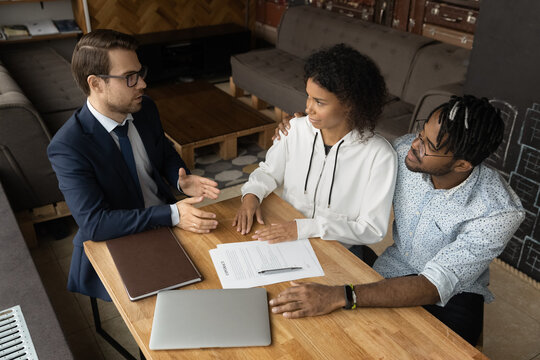 Capable young man lawyer bank manager consult interested african spouses customers by terms conditions of insurance contract. Black couple clients discuss purchase agreement details with broker expert