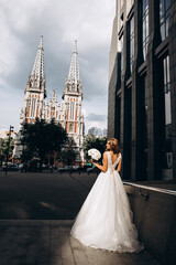 Obraz premium The bride in a white dress is holding a beautiful wedding bouquet. The bride on the background of the old cathedral.